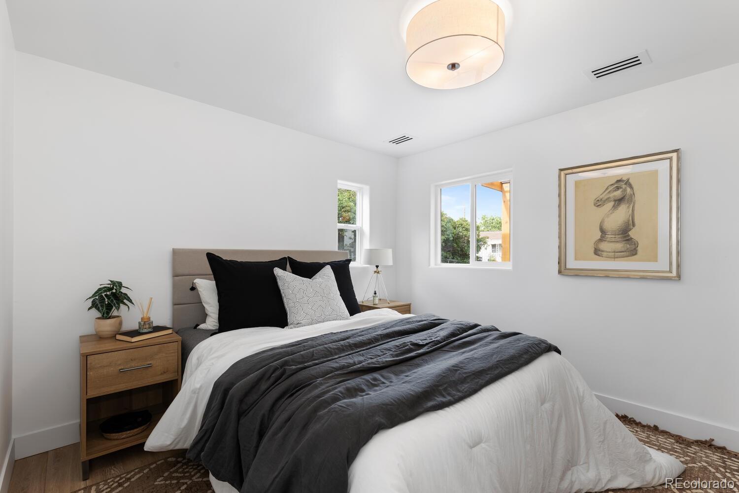 Staged bedroom with white bedding, a dark gray blanket, and framed horse artwork.