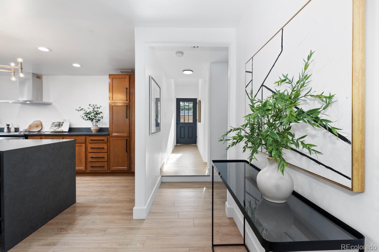 Entryway with a hallway to a dark blue front door beside a warm wood-cabinet kitchen.