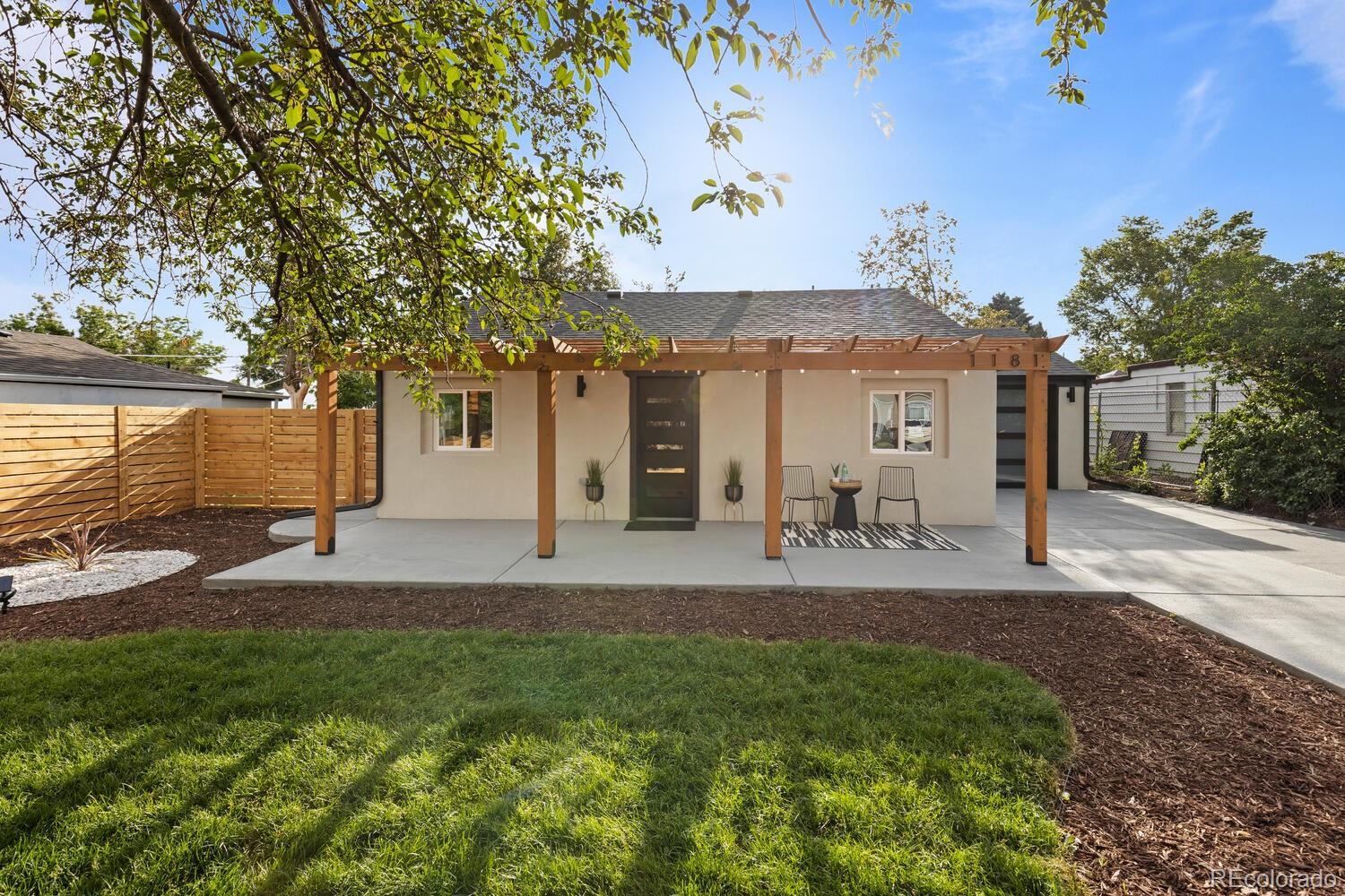 Home’s rear patio with a wooden pergola, outdoor seating, lawn, and privacy fence.
