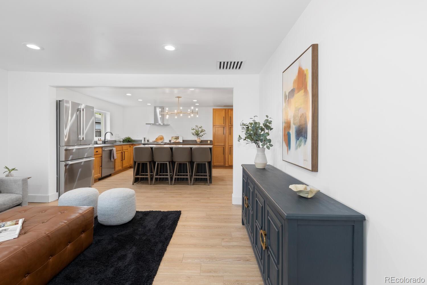 Open-plan living room and kitchen with a four-seat island, stainless steel appliances, and light wood floors.