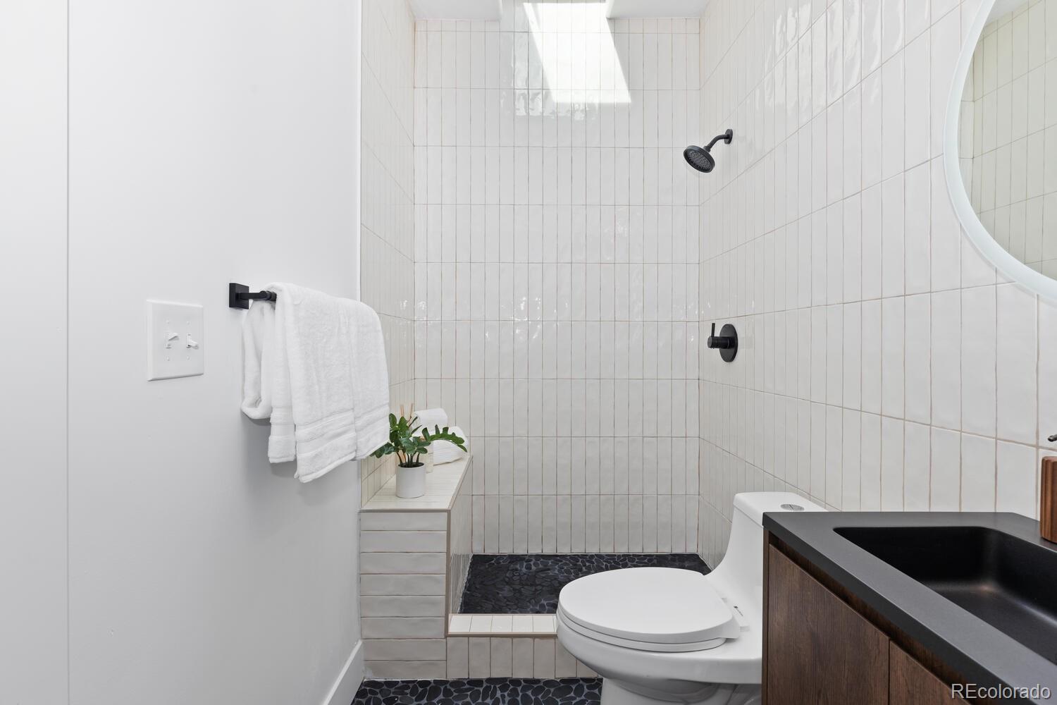 Modern bathroom with a white-tiled walk-in shower, dark pebble floor, and matte-black fixtures.