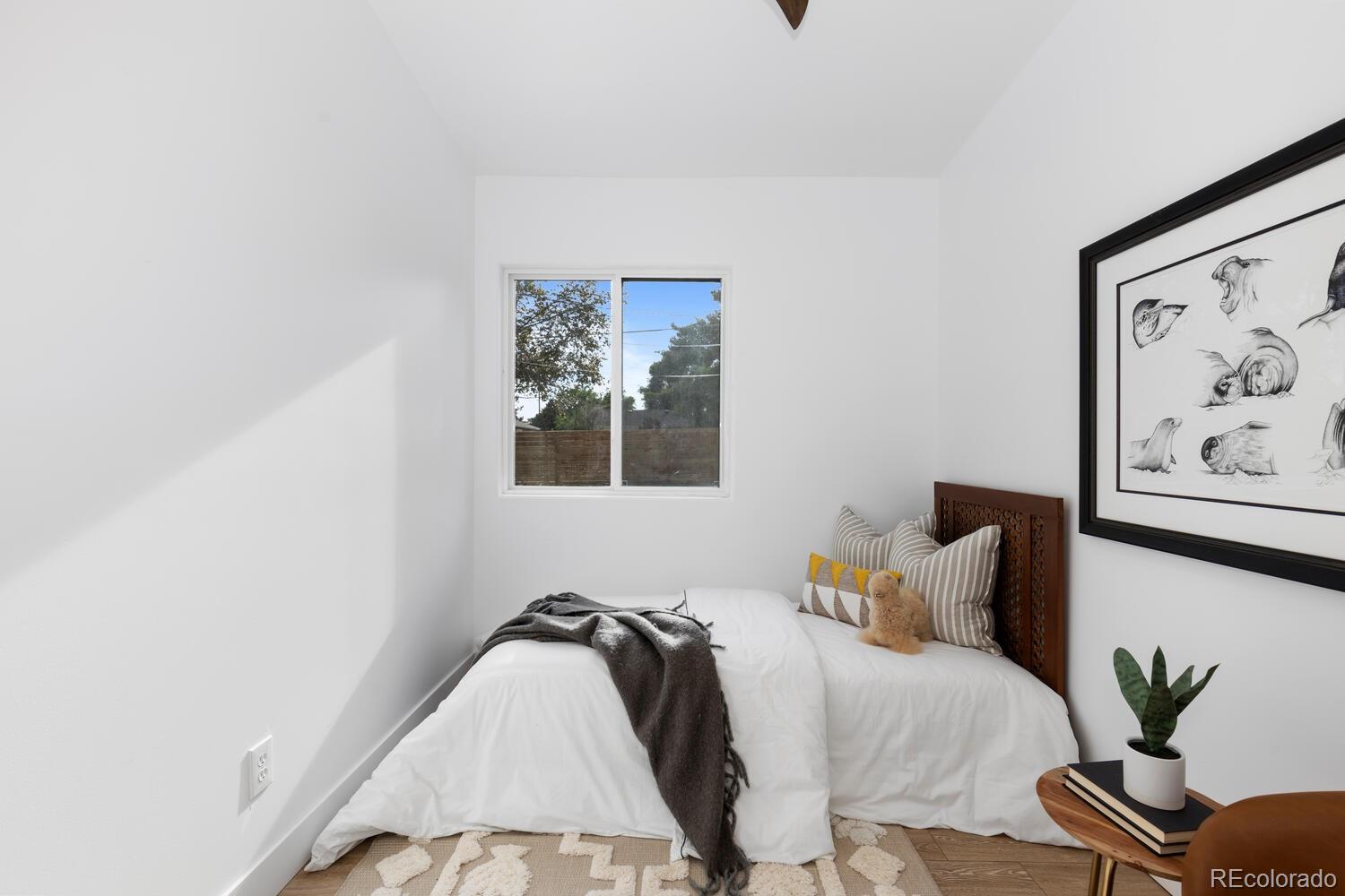 Staged bedroom with a white bed, dark throw, window, and framed animal sketches.
