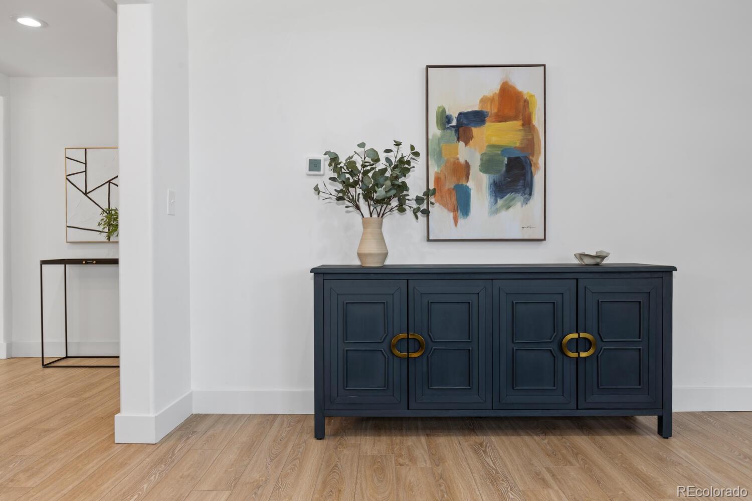 Staged entryway with a dark blue console cabinet, colorful abstract artwork, and light wood flooring.