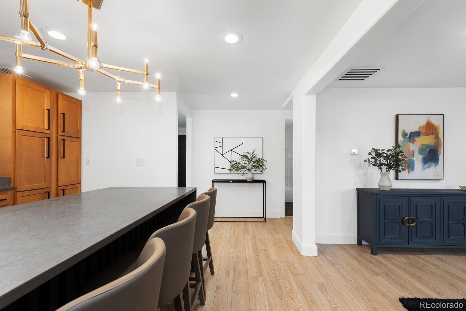 Kitchen with a long gray island, wood cabinetry, counter stools, and brass pendant lighting.