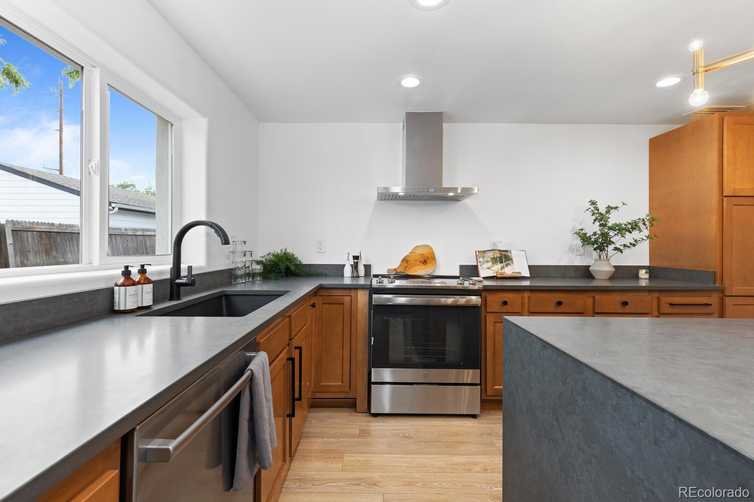Kitchen with warm wood cabinets, gray counters, stainless appliances, and a large window.