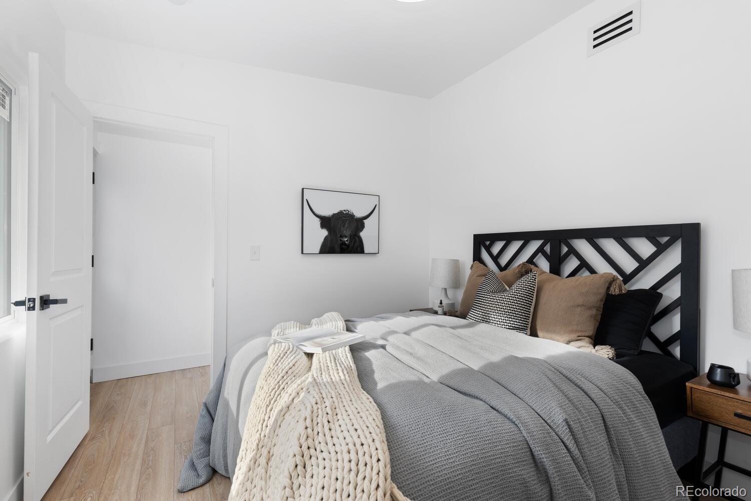 Bedroom with a black geometric headboard, layered gray bedding, and framed Highland cow artwork.