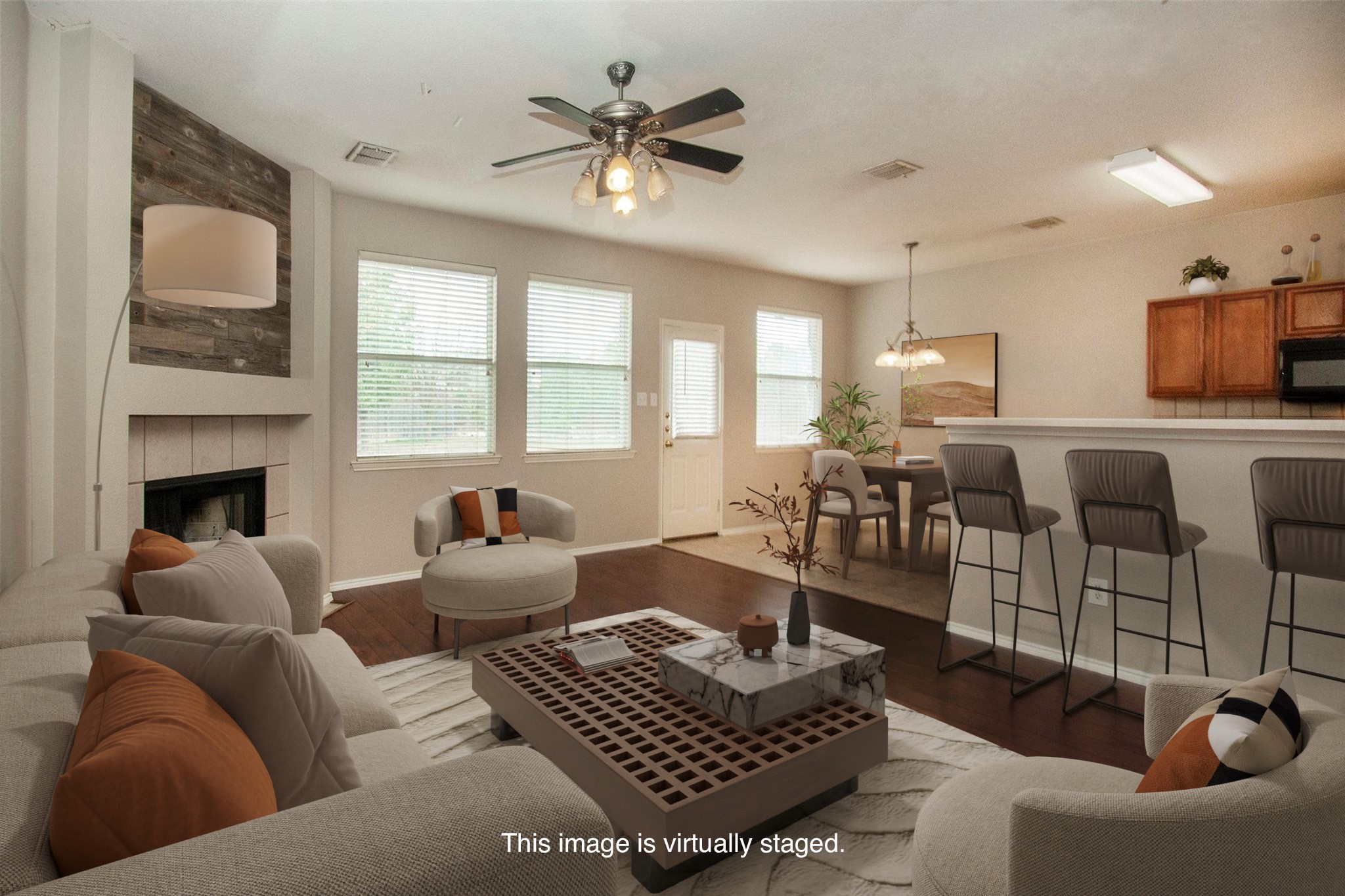 Virtually staged living room with a fireplace, wood floors, and an open kitchen with breakfast bar.