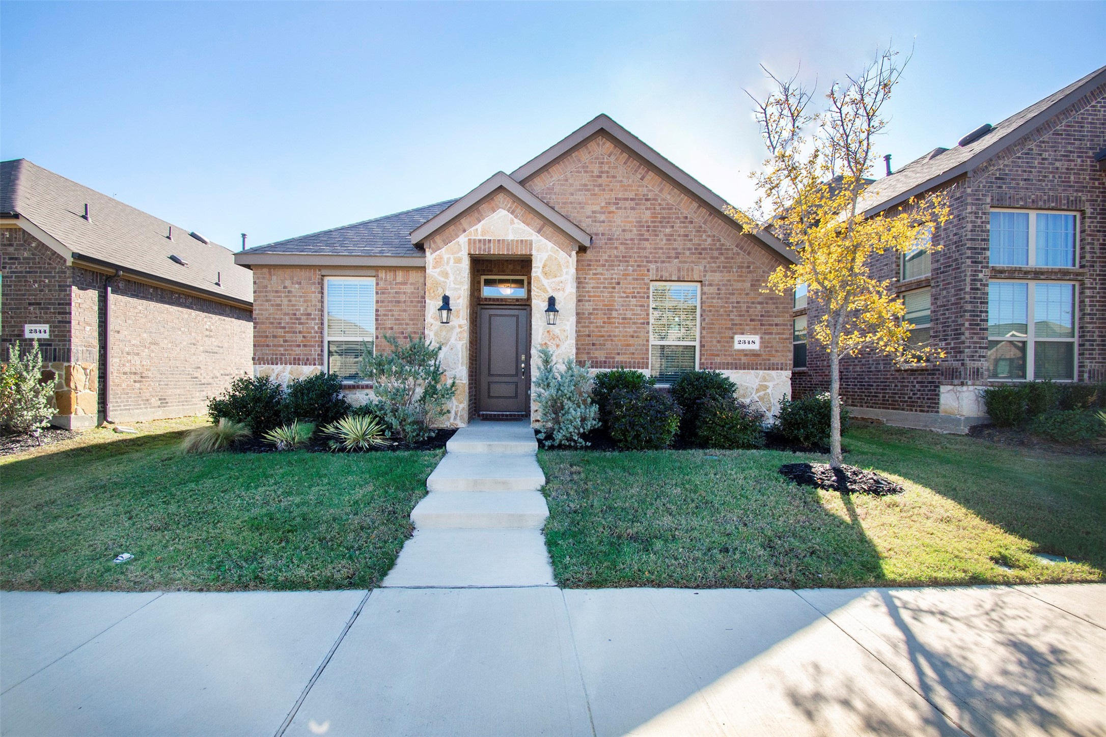 Brick house with a stone entry, landscaped lawn, and yellow-leaved tree.