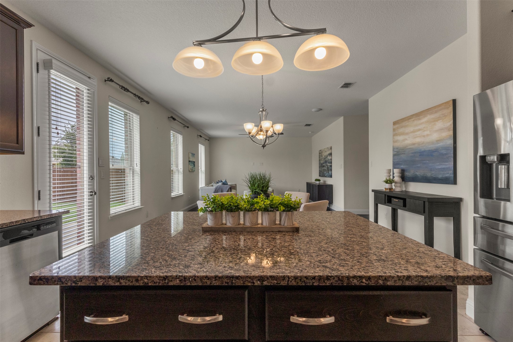 Kitchen with a large granite island, stainless steel appliances, and pendant lights overlooking the dining area.