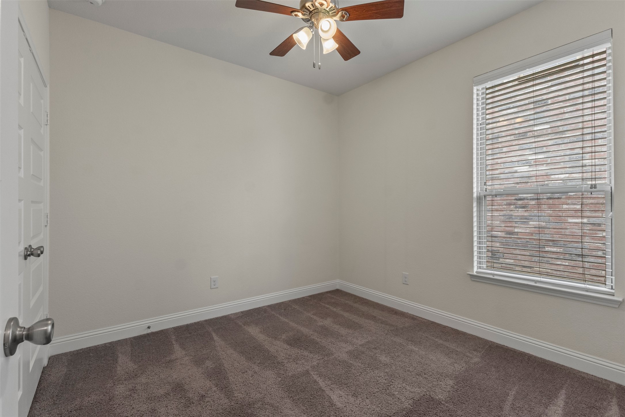 Empty bedroom with brown carpet, a ceiling fan, and a window with white blinds.