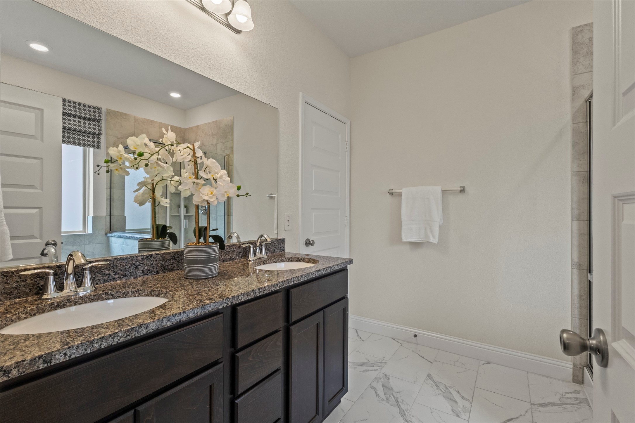 Bathroom with dark double vanity, granite countertop, white orchids, and marble-look tile floor.