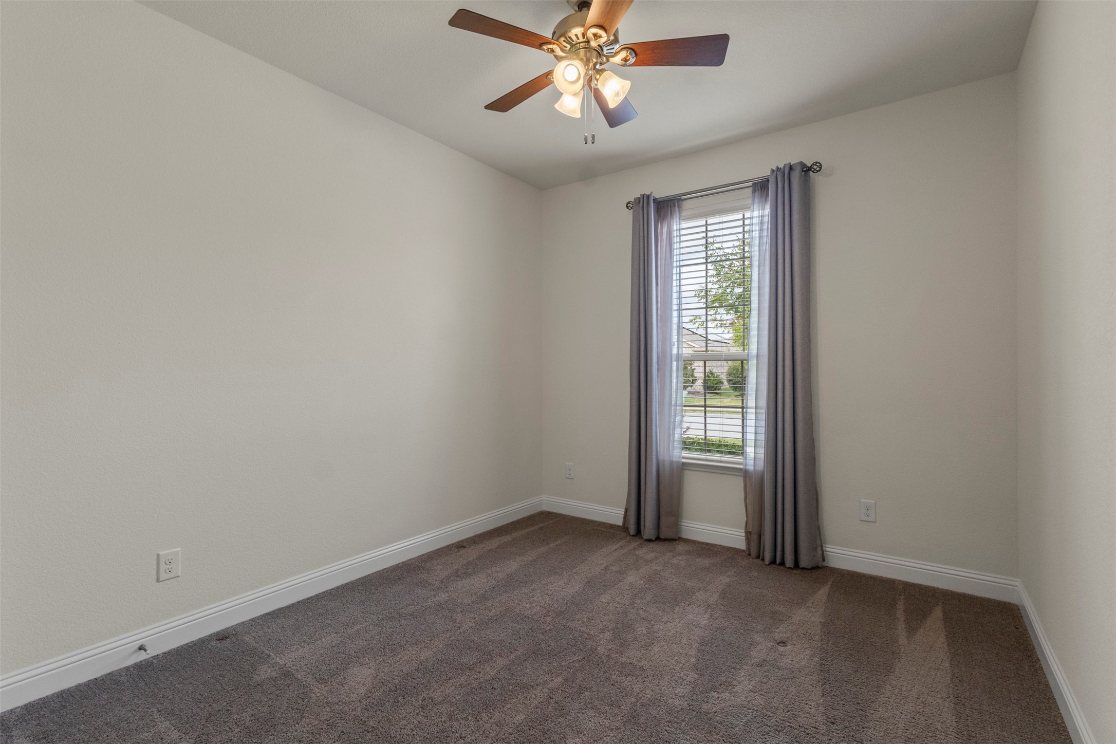 Empty carpeted bedroom with a ceiling fan and a curtained window.