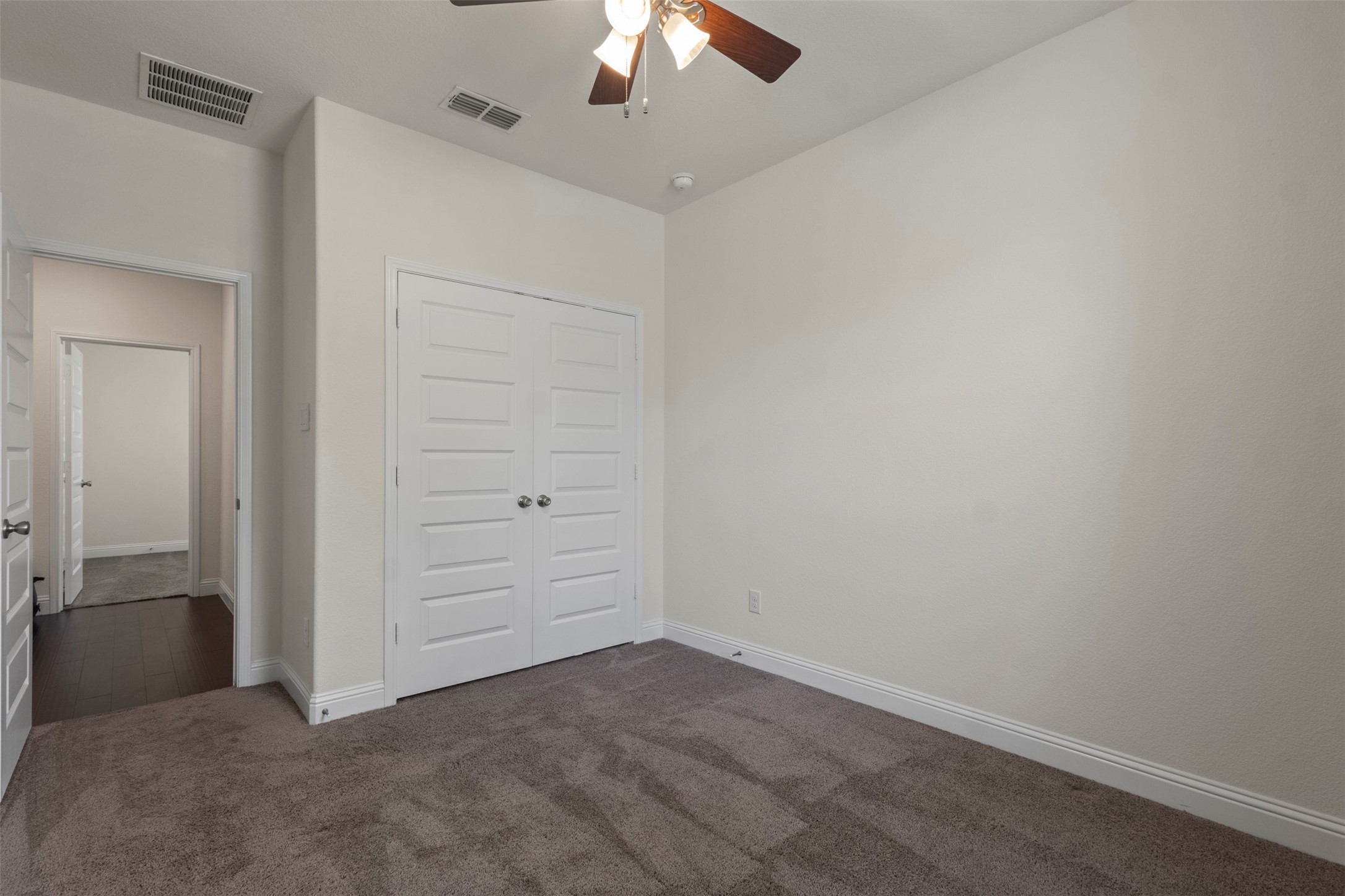 Empty bedroom with taupe carpet, white double closet doors, and a ceiling fan