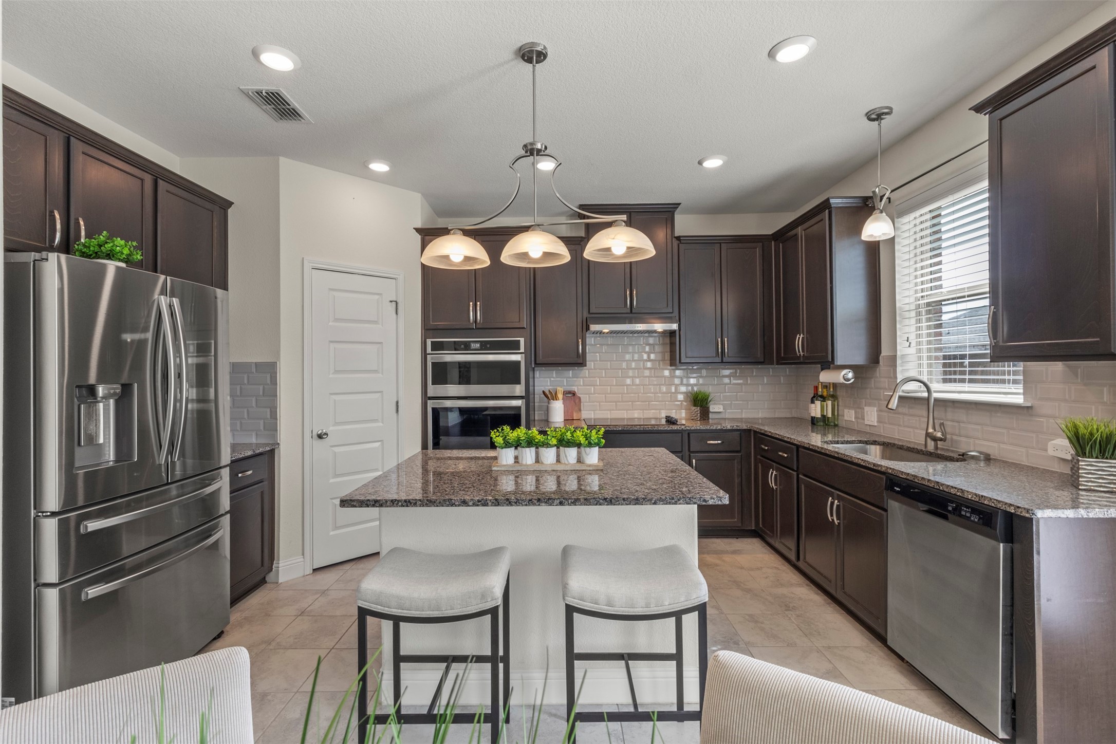 Kitchen with dark cabinets, stainless steel appliances, and a stone island with two stools.