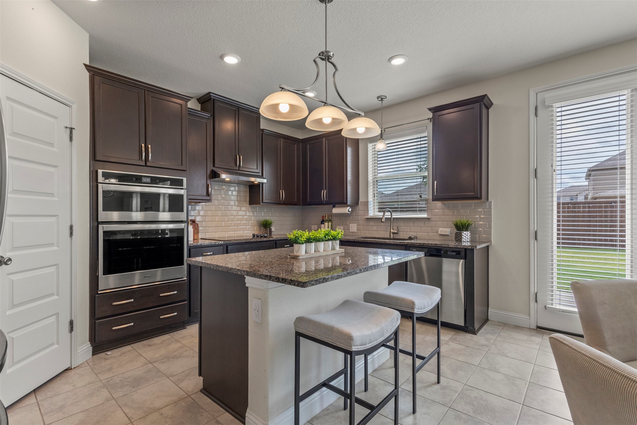 Kitchen with dark cabinets, stainless steel double ovens, and a granite island with two stools.