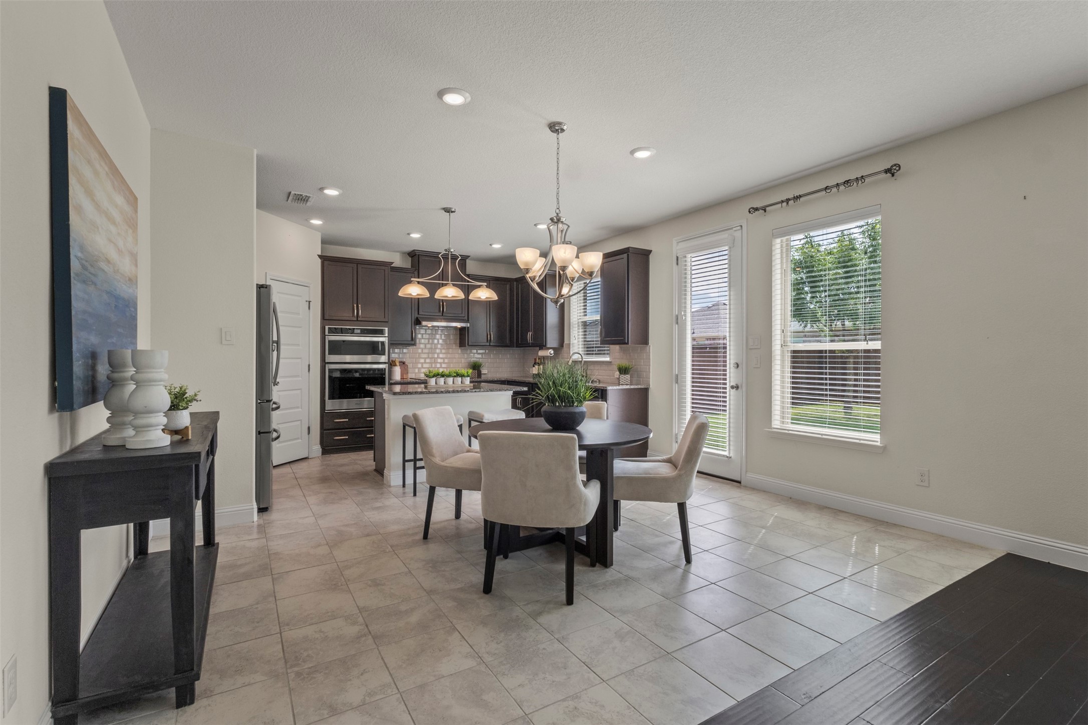 Open-plan kitchen and dining area with dark cabinetry, stainless appliances, and a round table by the windows.