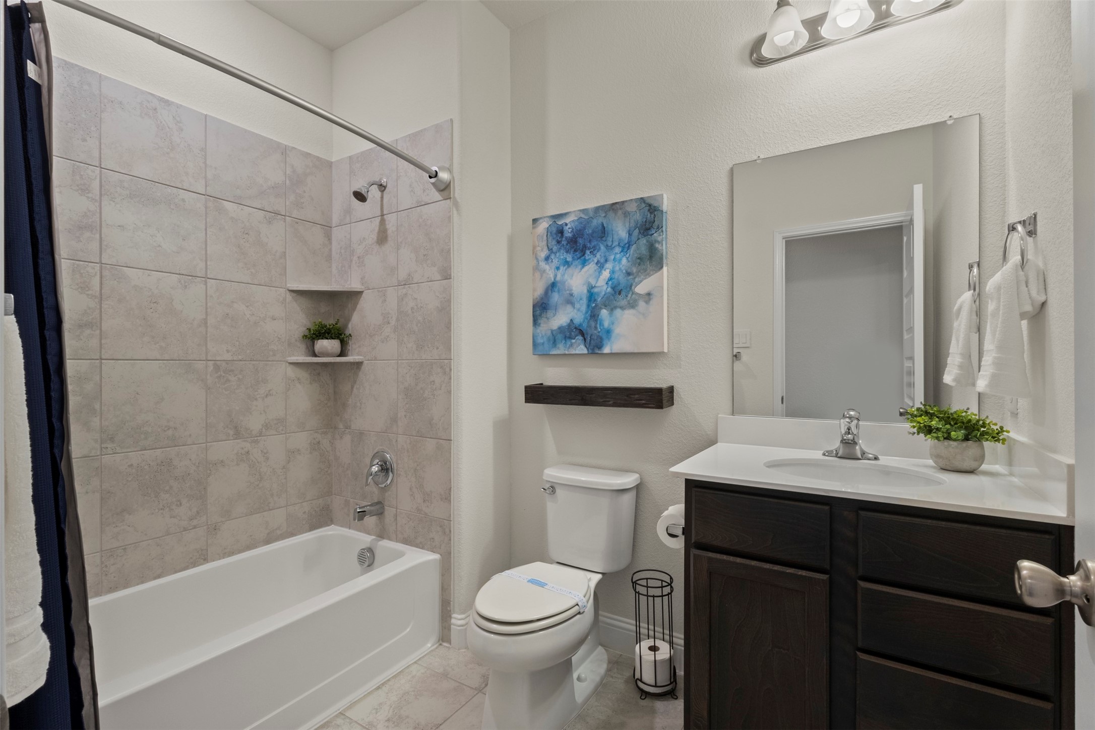 Bathroom with tiled tub and shower, dark wood vanity, and blue abstract wall art.
