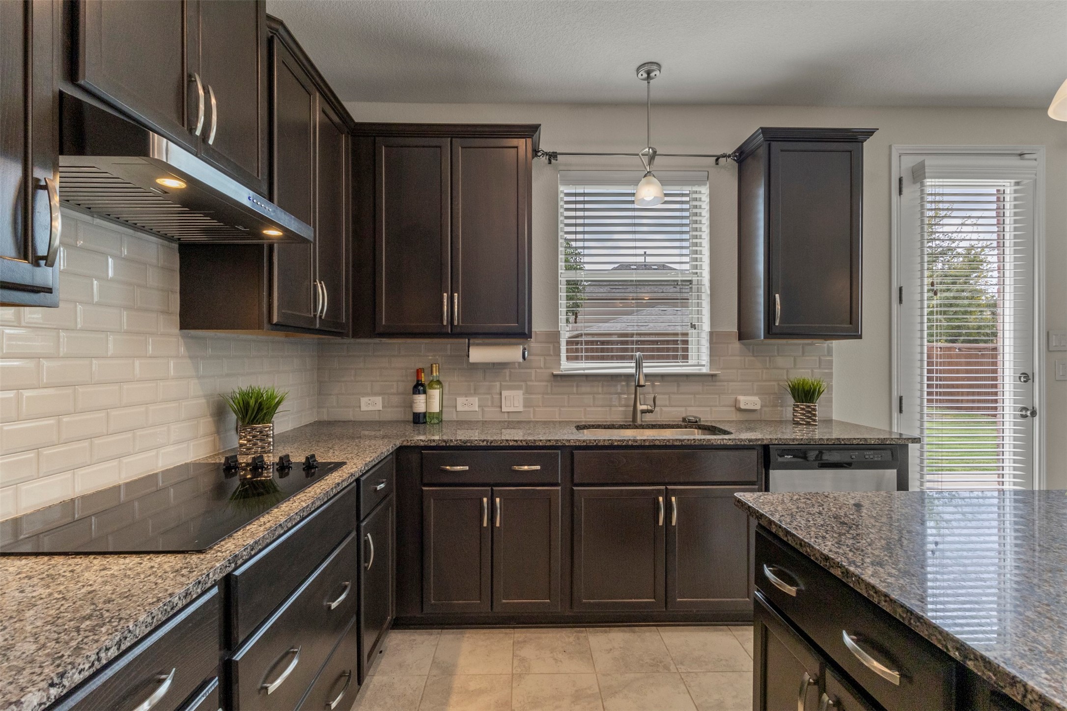 Kitchen with dark wood cabinets, granite counters, white tile backsplash, and an island.