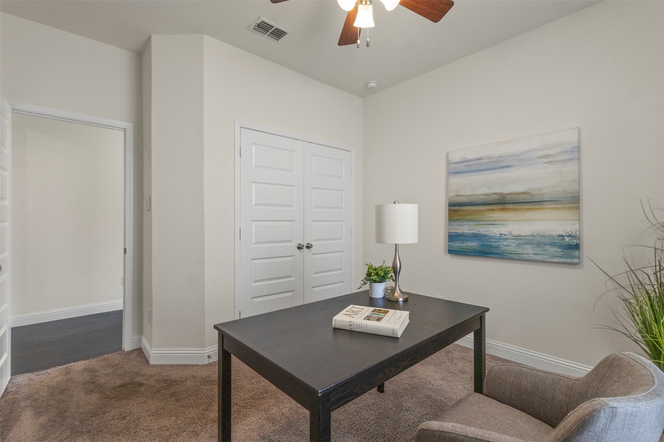 Furnished home office with a dark desk, gray chair, and blue-toned abstract artwork.