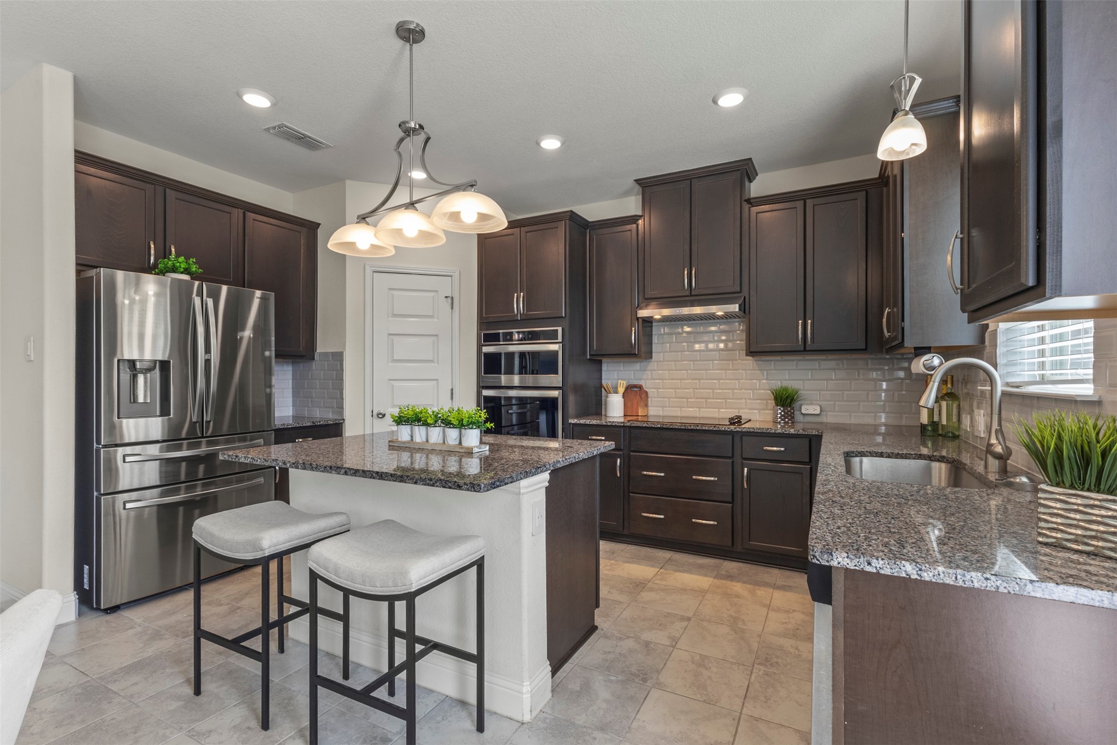 Kitchen with dark cabinets, granite island and counters, stainless steel appliances, and two stools.