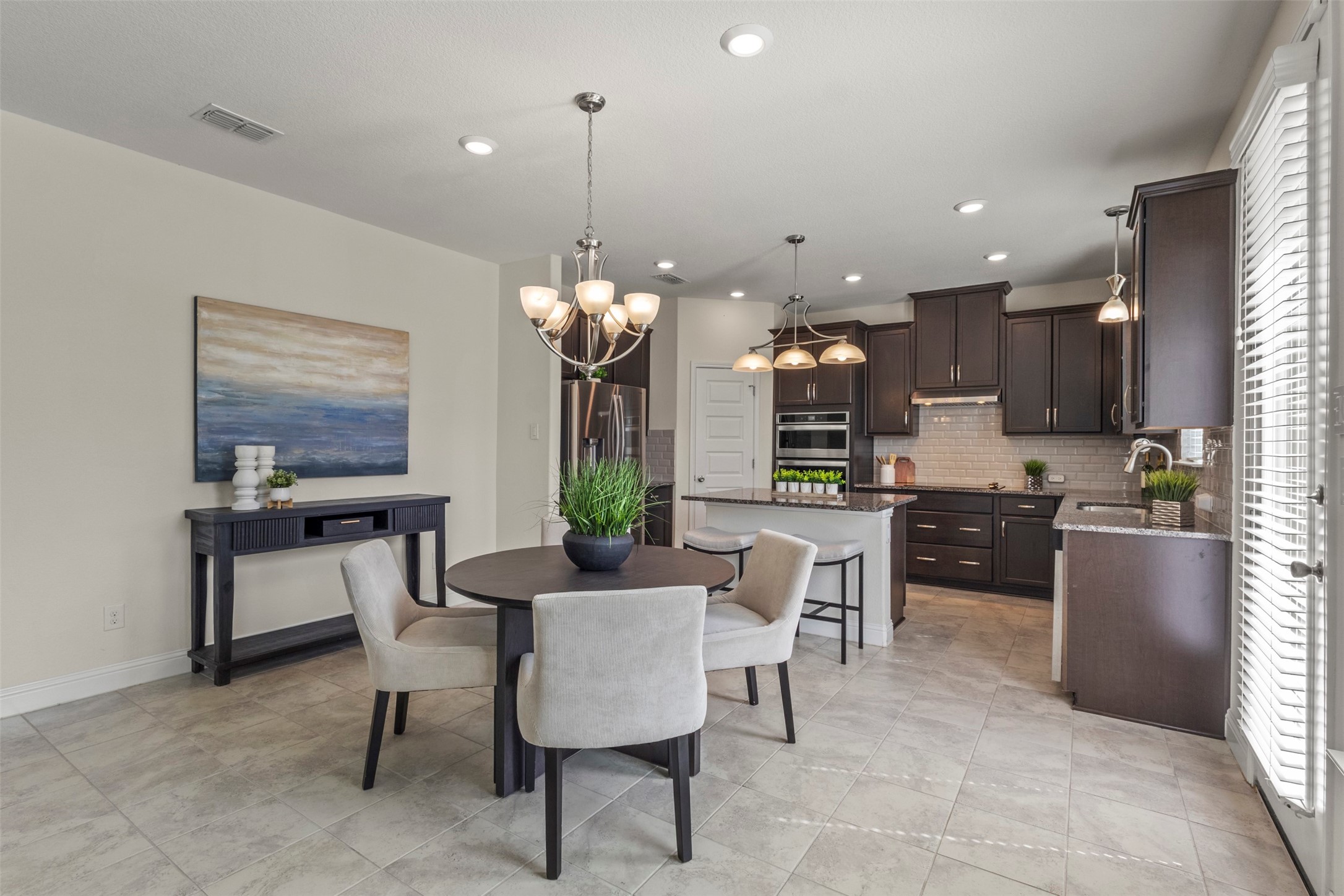 Open-plan kitchen and dining area with dark cabinets, a stone island, and a round table with upholstered chairs.