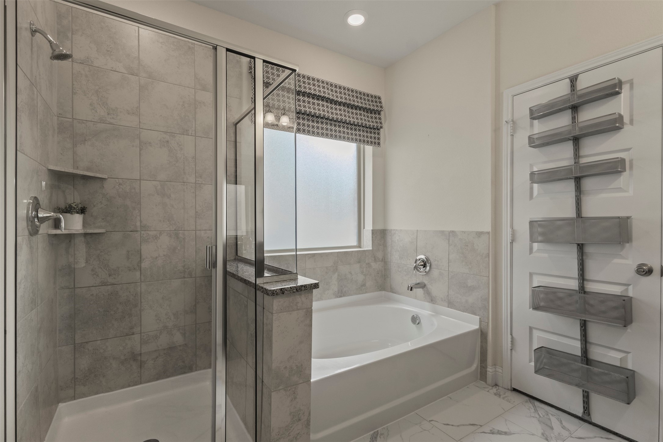 Bathroom with a glass-enclosed tiled shower, soaking tub, and door-mounted storage racks.