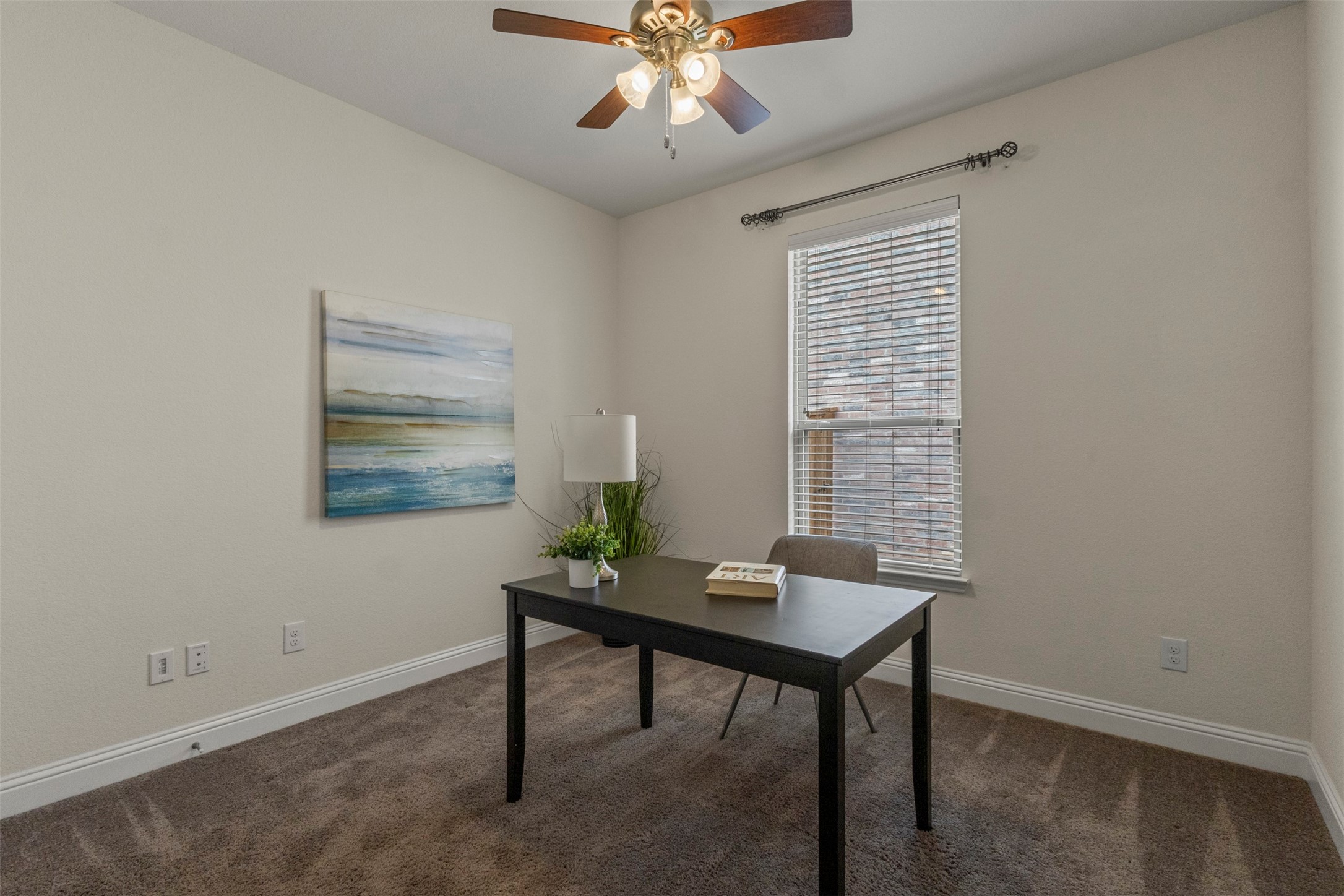 Staged home office with a dark desk, carpet, window blinds, and ceiling fan.
