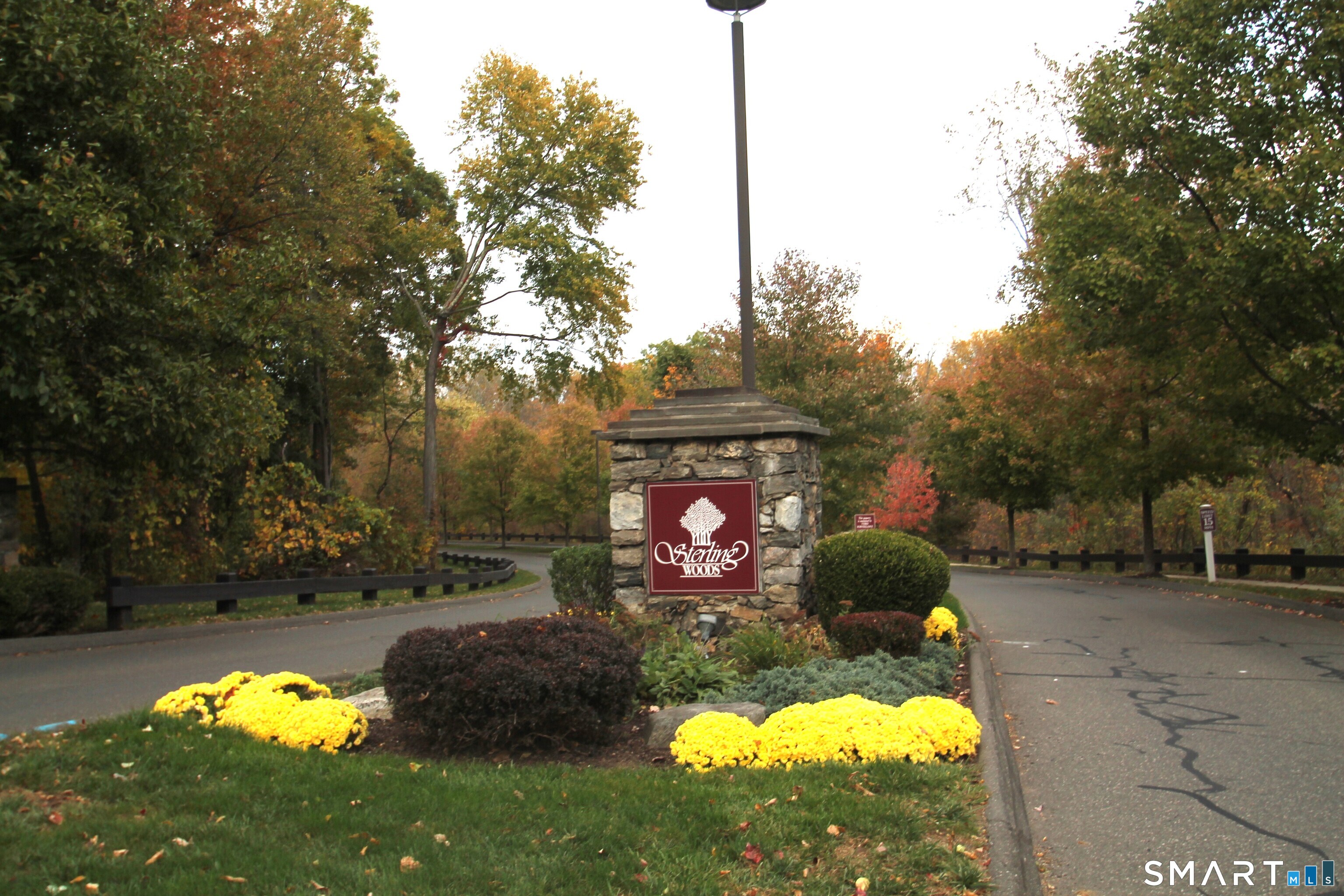 Sterling Woods entrance sign on a stone monument beside a landscaped road in autumn.