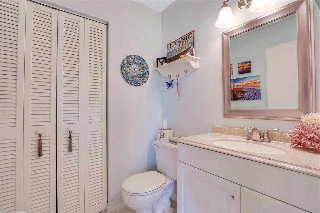 Bathroom with a white vanity, large mirror, toilet, and louvered closet doors.
