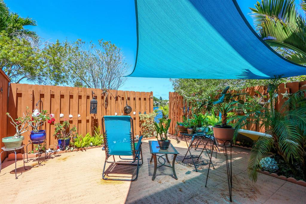 Fenced patio with a turquoise shade sail, potted plants, and blue seating.