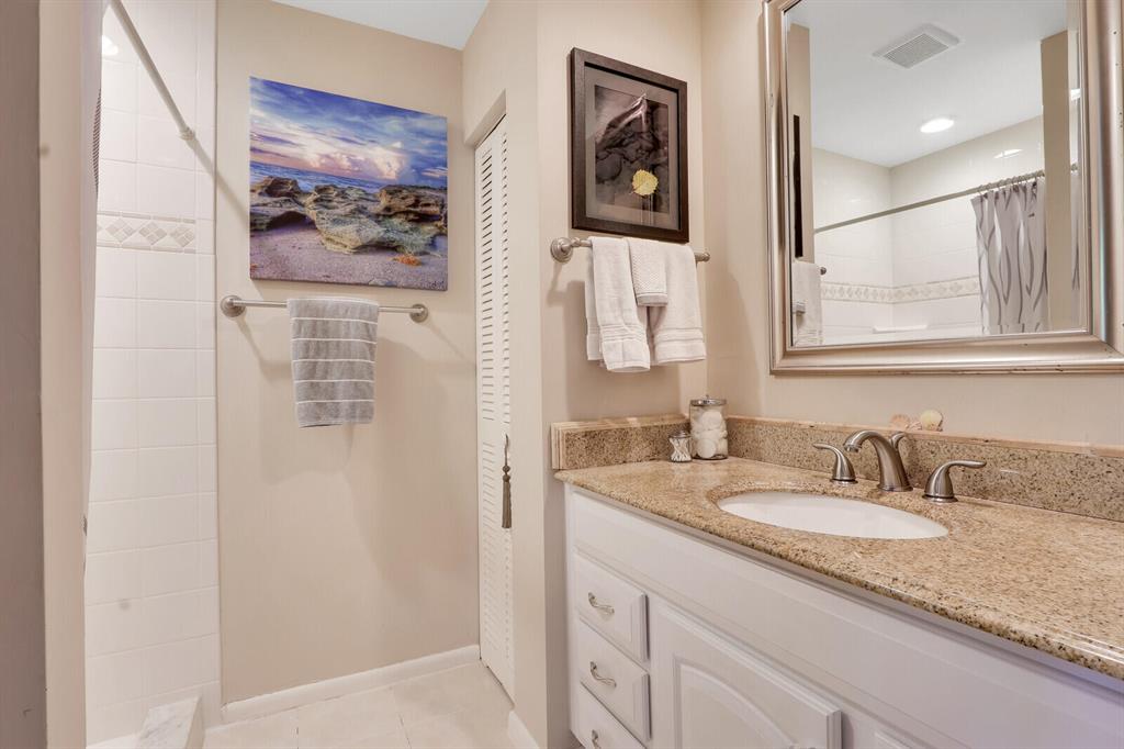 Bathroom with a white vanity, granite countertop, large mirror, and coastal artwork.