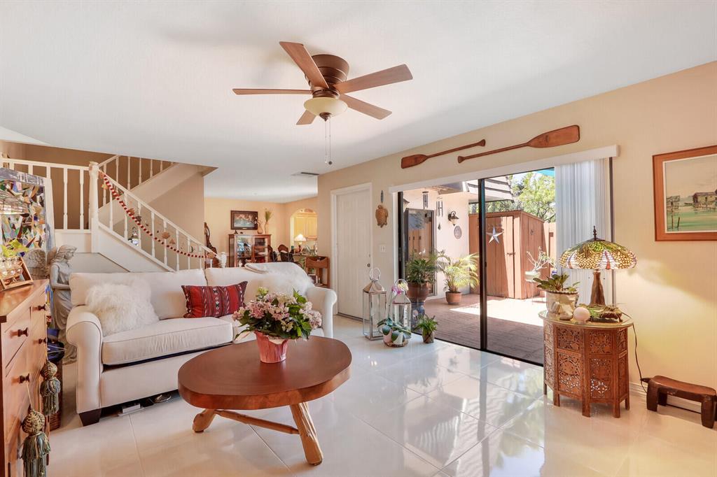 Living room with white sofas, a staircase, and sliding doors opening to a sunny patio.