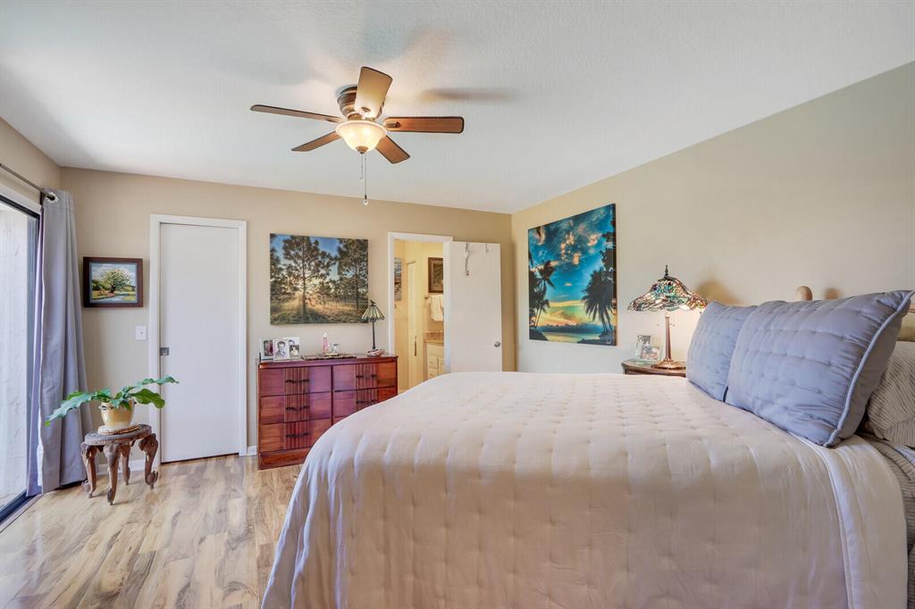 Bedroom with a large light-quilted bed, blue pillows, ceiling fan, and tropical wall art.