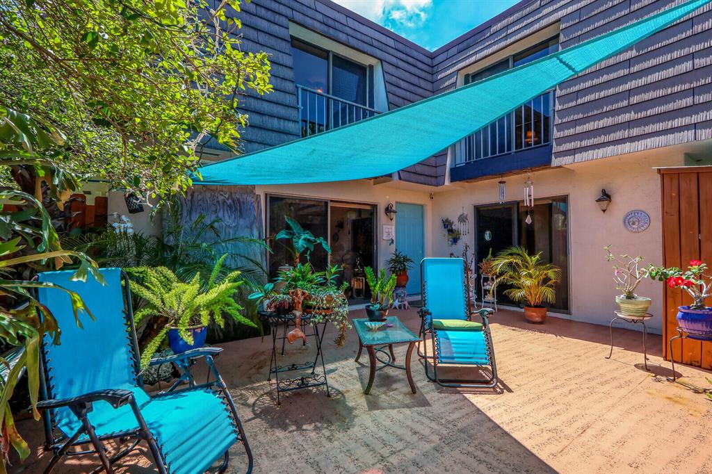 Courtyard patio with turquoise lounge chairs, a shade sail, and potted plants beside the home.