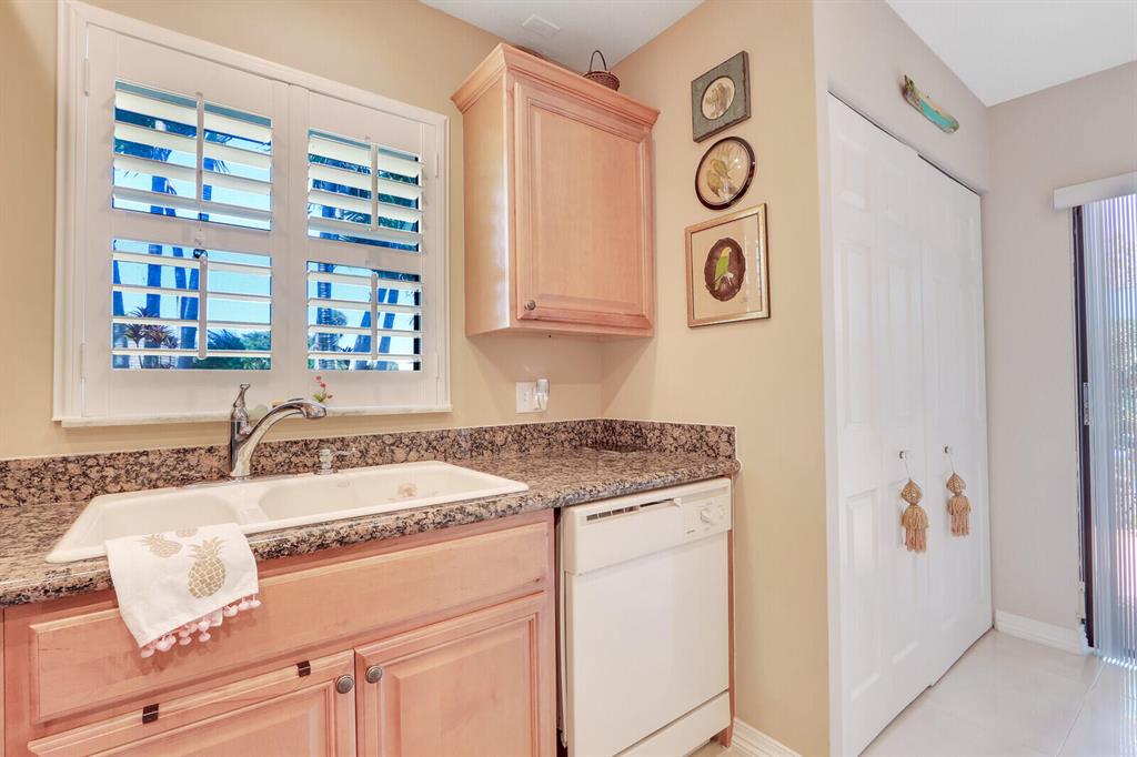 Compact kitchen with granite counters, light wood cabinets, and a sink beneath plantation shutters.