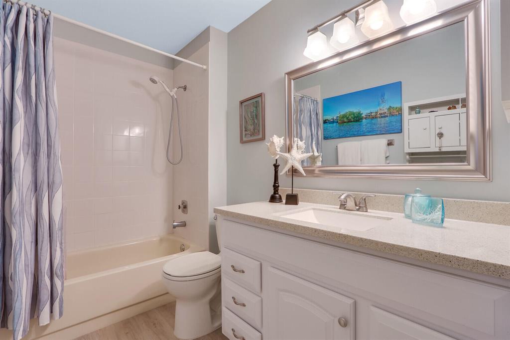Bathroom with a white bathtub, patterned shower curtain, toilet, and long vanity beneath a large mirror.