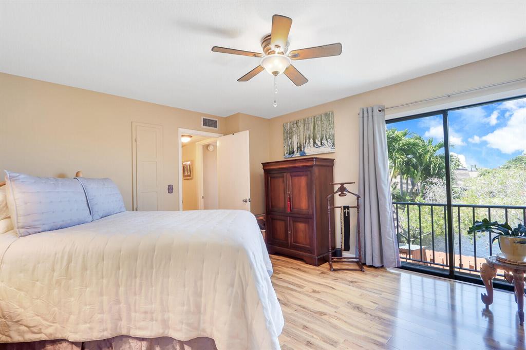 Bedroom with white bedding, a wooden armoire, and sliding doors overlooking leafy trees.
