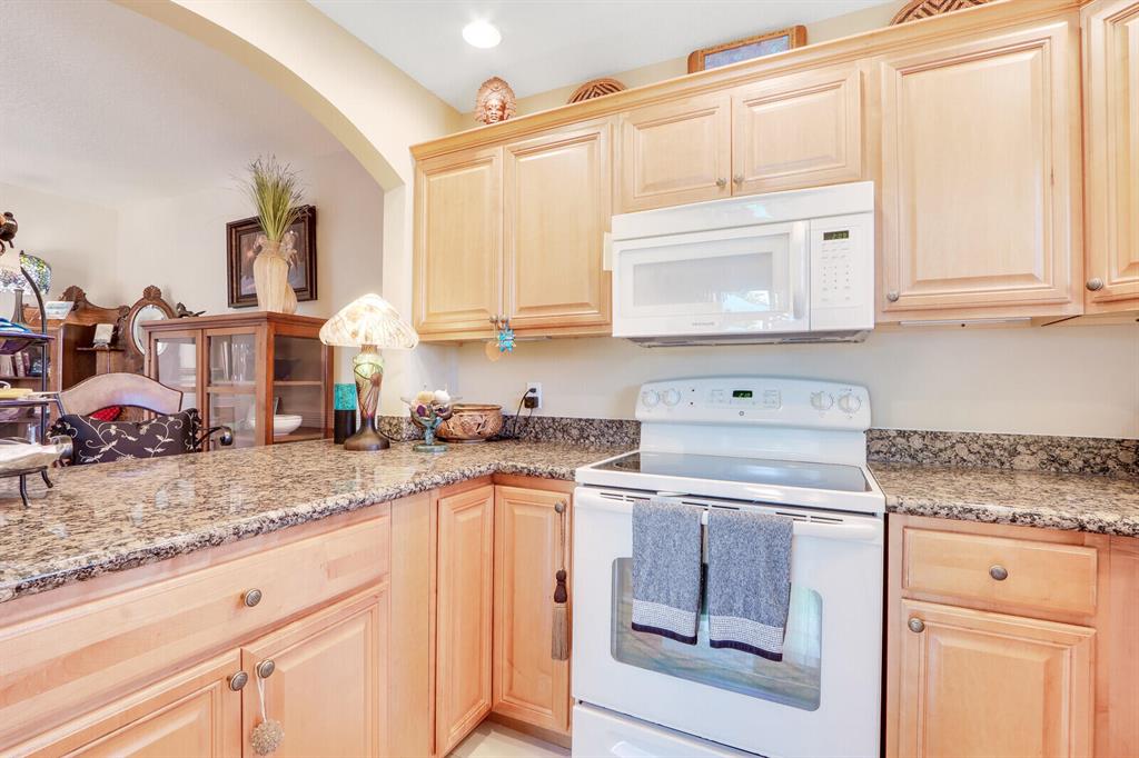 Kitchen with light wood cabinets, granite countertops, and white range and microwave.