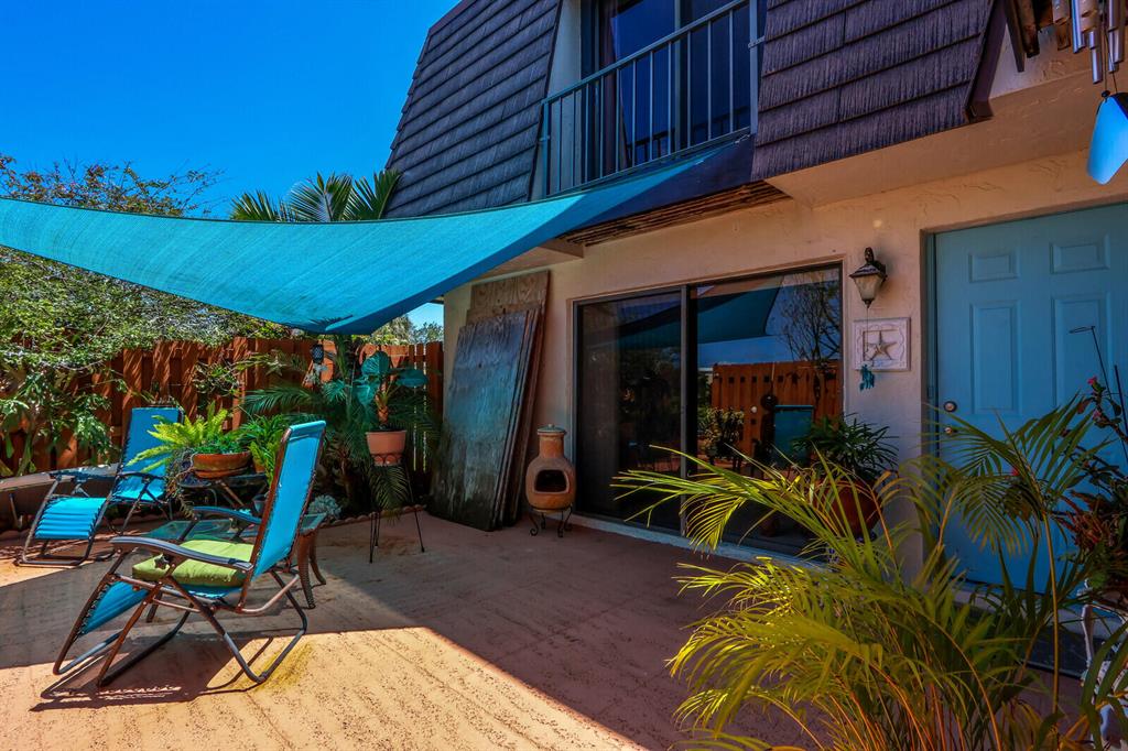 Home patio with a turquoise shade canopy, reclining chairs, tropical plants, and a clay chiminea.