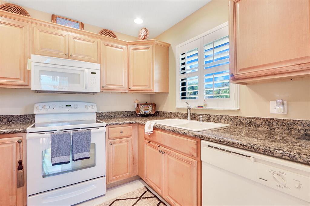 Kitchen with wood cabinets, granite counters, and a sink beneath shuttered windows.