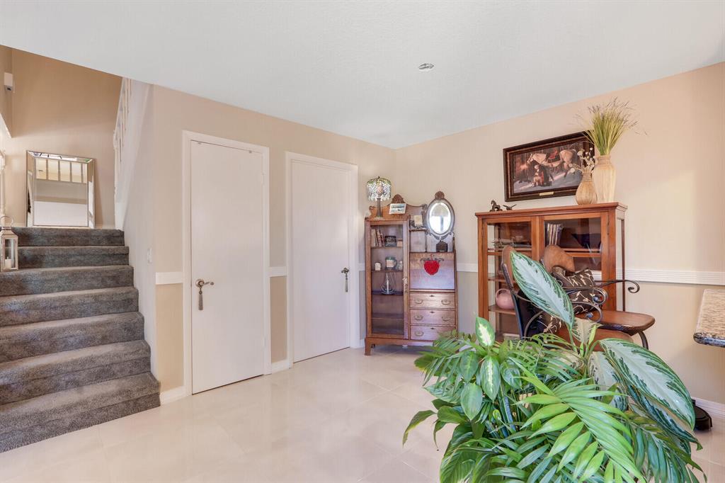 Furnished entryway with a carpeted staircase, wooden cabinets, and large leafy plants.