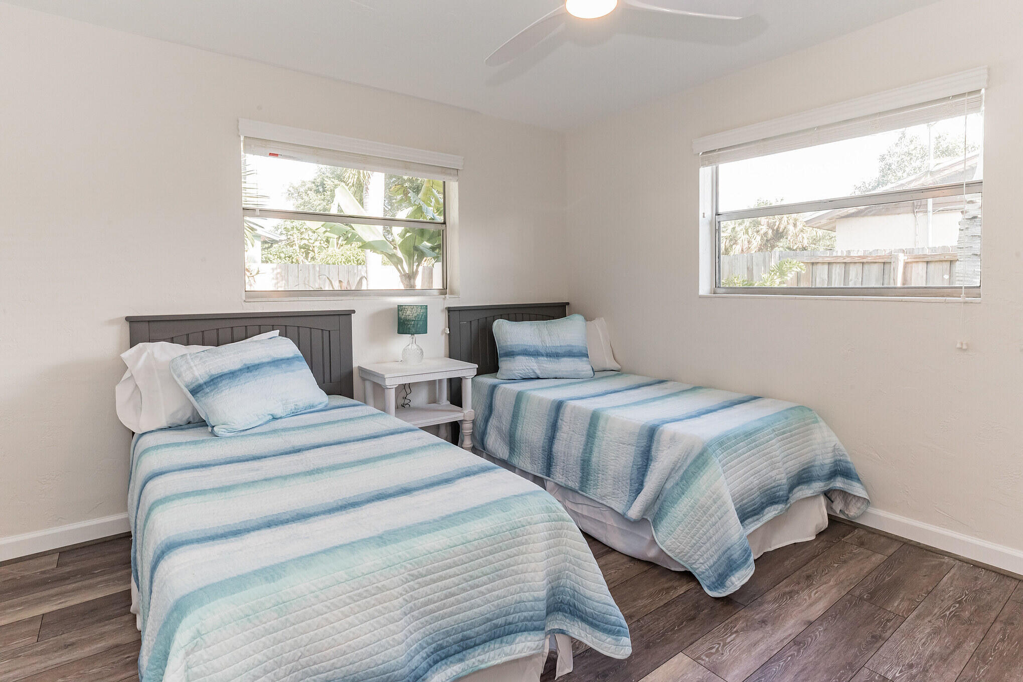 Bedroom with two twin beds in blue-and-white striped bedding and large windows.