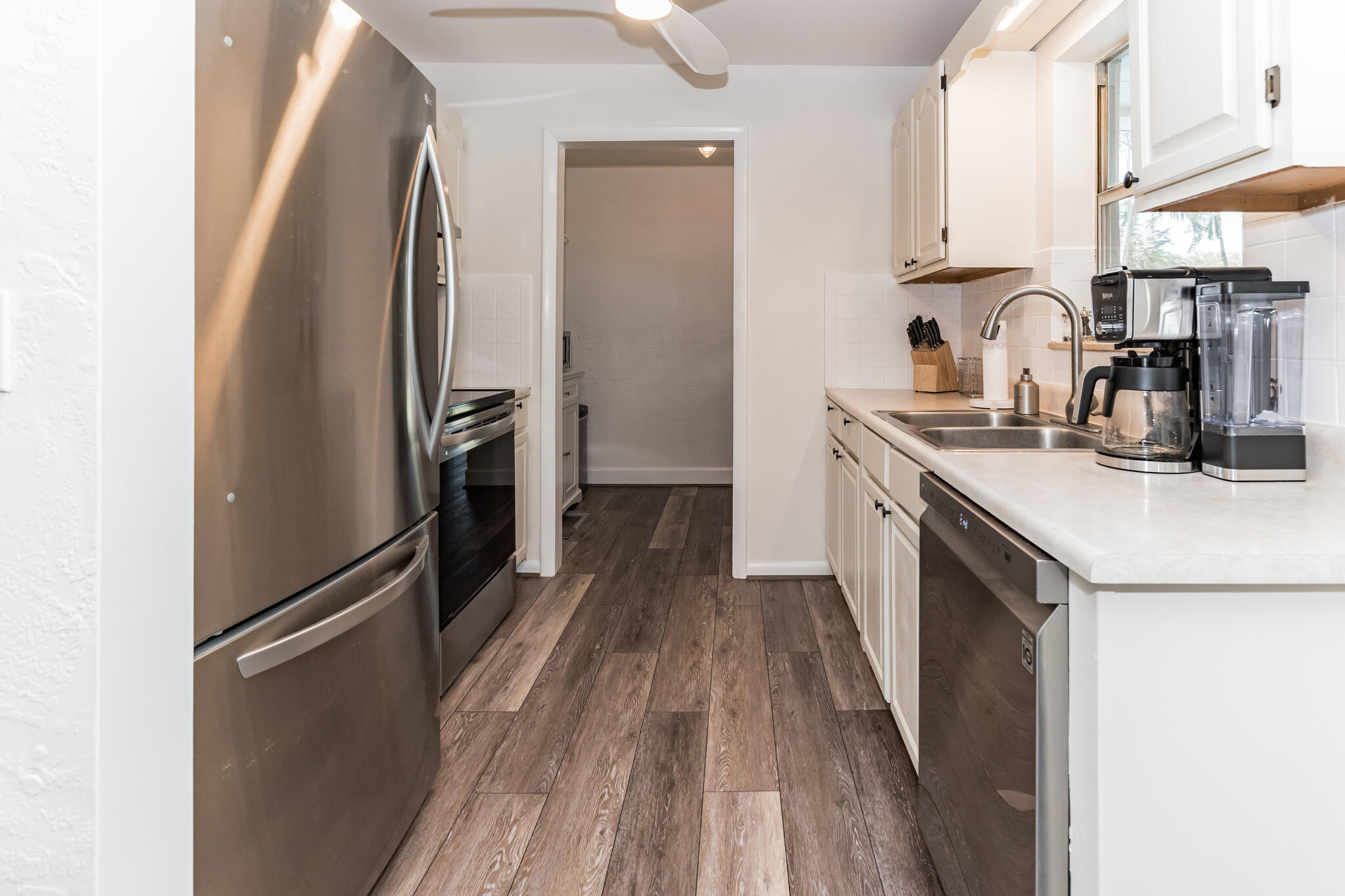 Kitchen with white cabinetry, stainless steel appliances, double sink, and dark plank flooring.