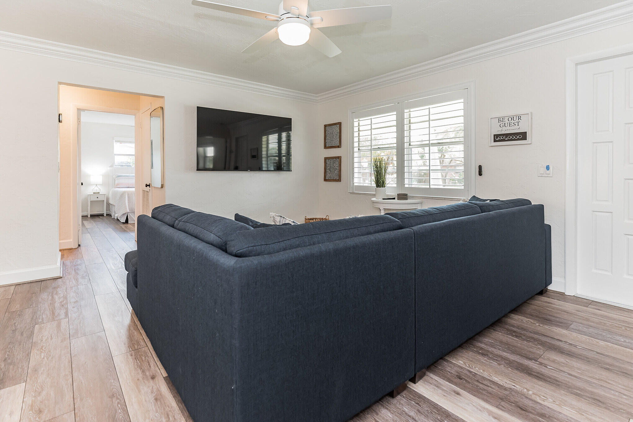 Living room with a dark blue sectional, wall-mounted TV, and plantation shutters.