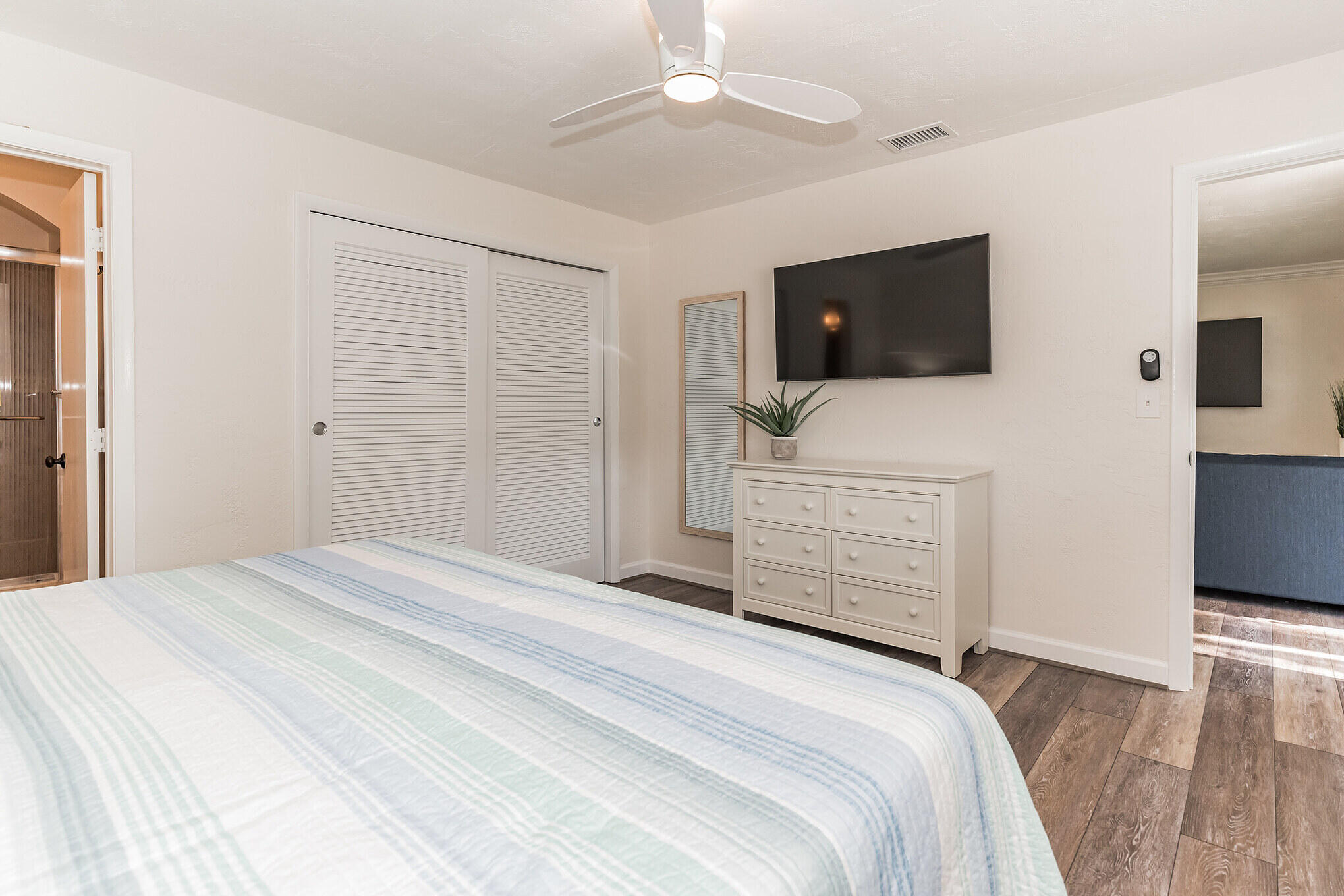 Bedroom with pale striped bedding, louvered closet doors, and a wall-mounted television.