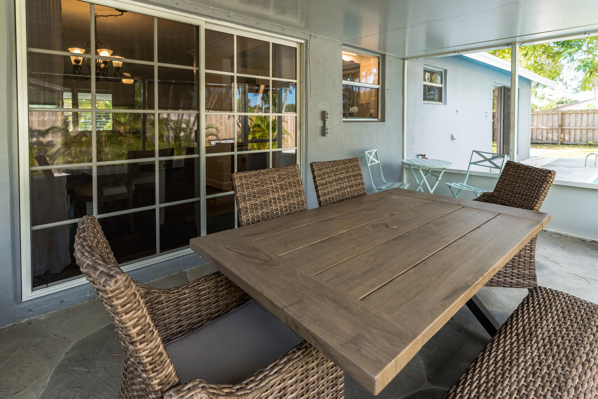Covered patio with a wooden dining table, woven chairs, and a glimpse of the pool.