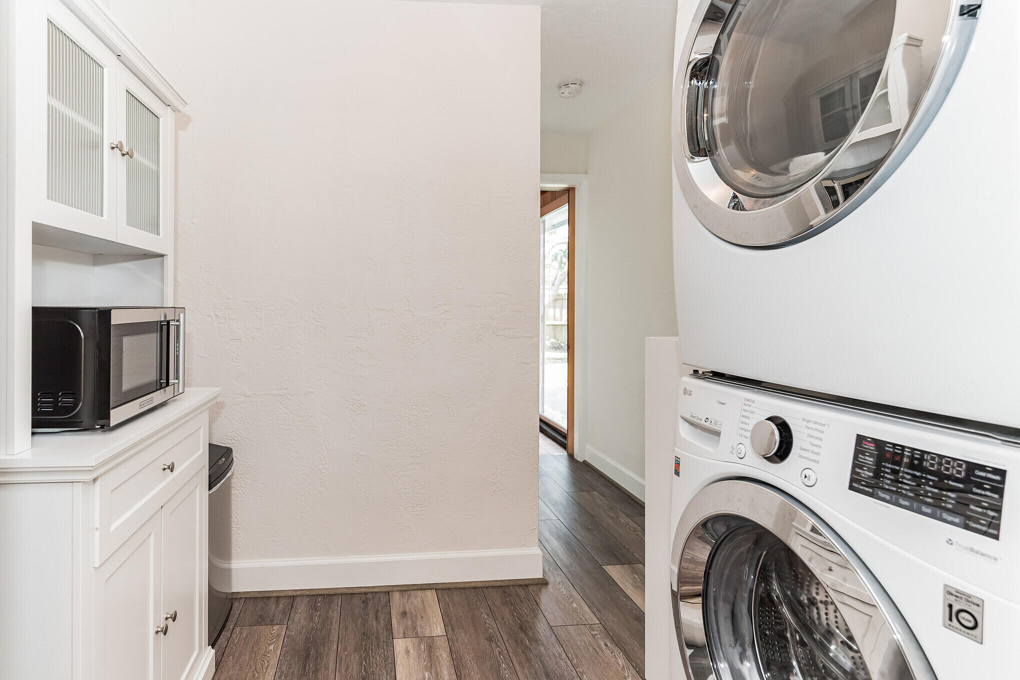 Laundry area with stacked front-loading washer and dryer, white cabinetry, and a microwave.