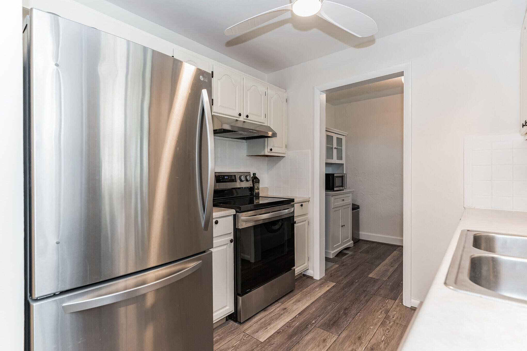 Kitchen with white cabinets, stainless steel appliances, a double-basin sink, and dark wood-look flooring.
