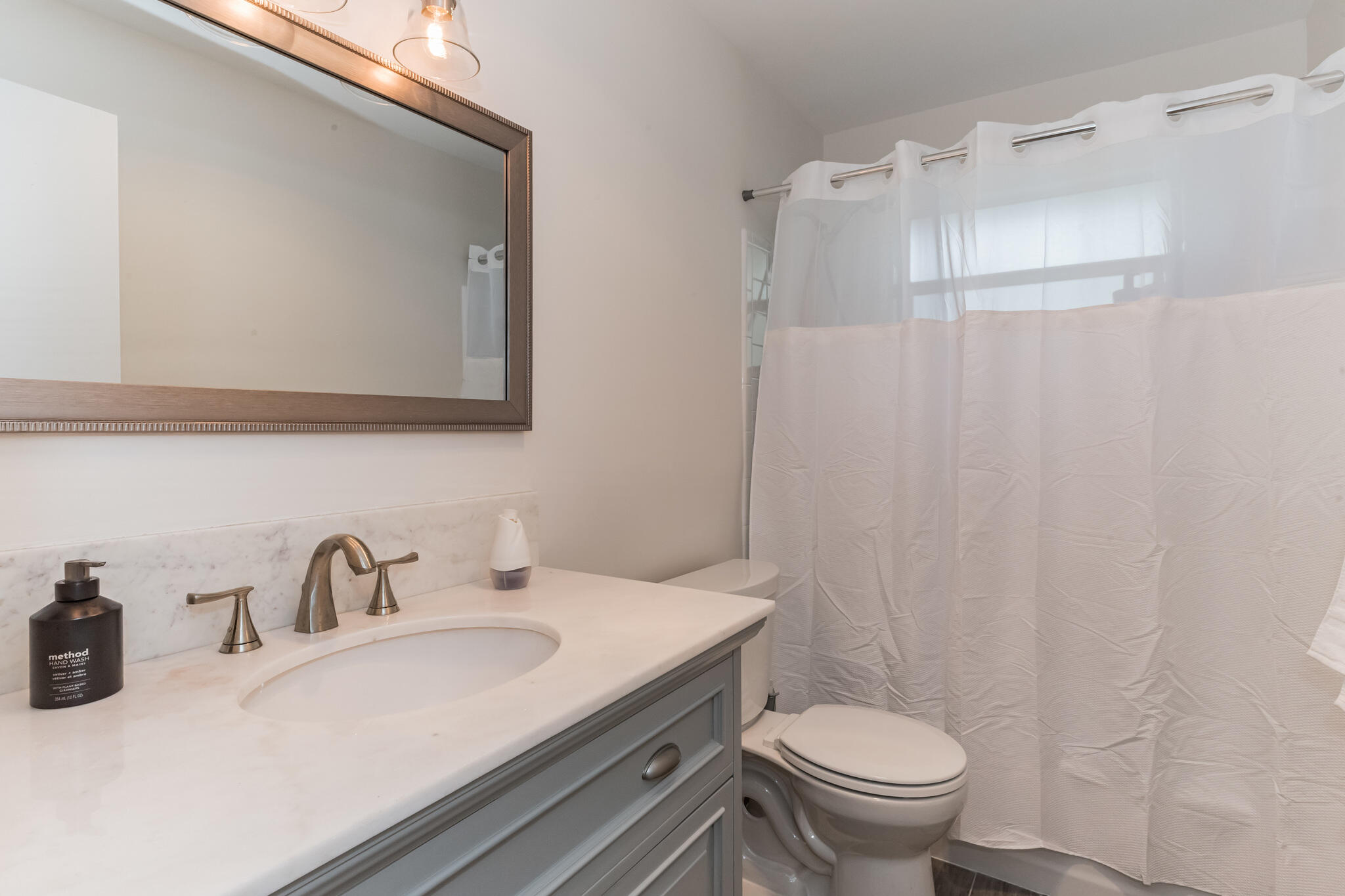 Bathroom with a marble-look vanity, gray cabinetry, and a white shower curtain.