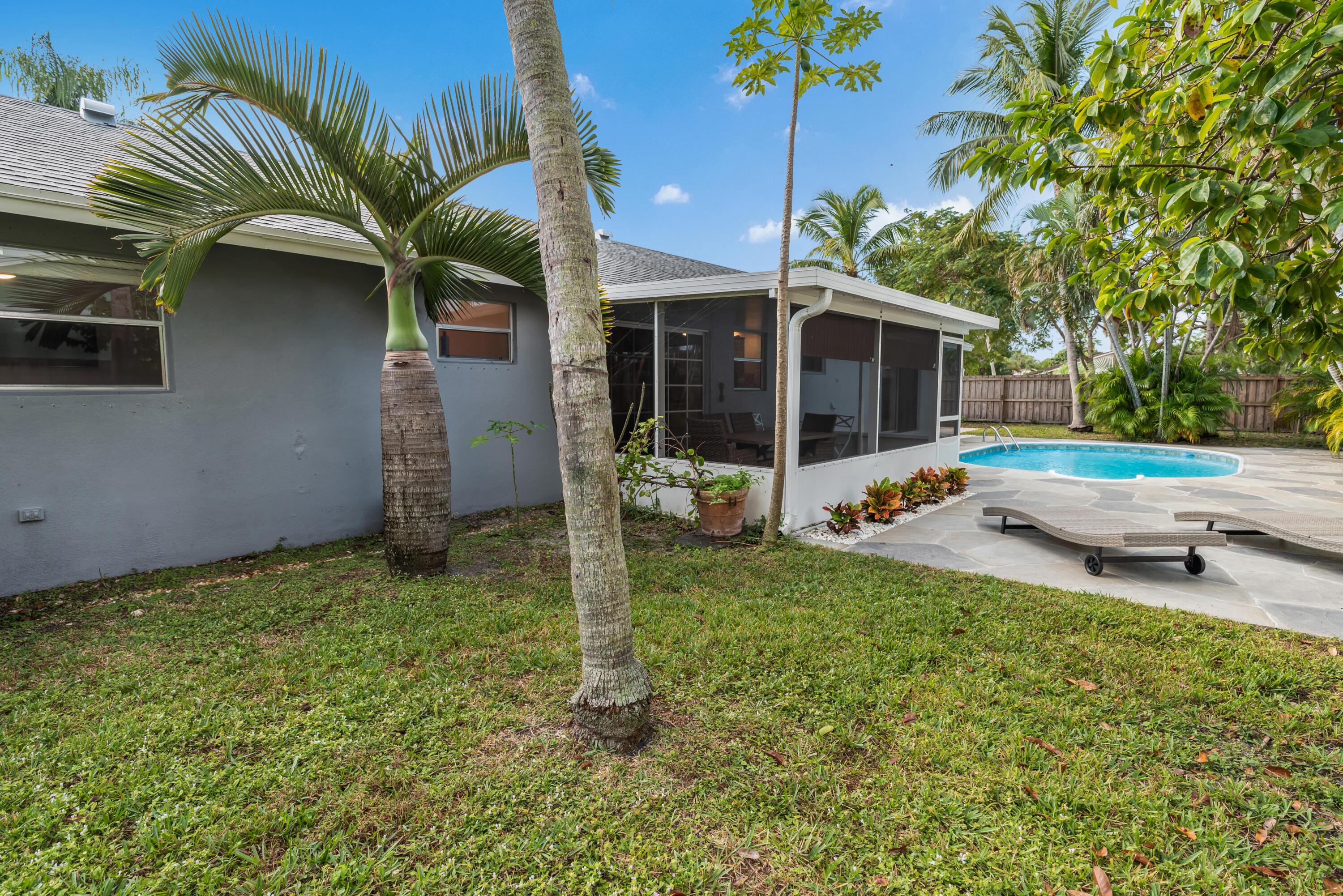 Gray home with a screened patio beside a backyard pool, palm trees, and stone paving.